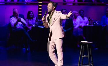 Comedy vs Cancer host Nick Kroll on stage holding a microphone.