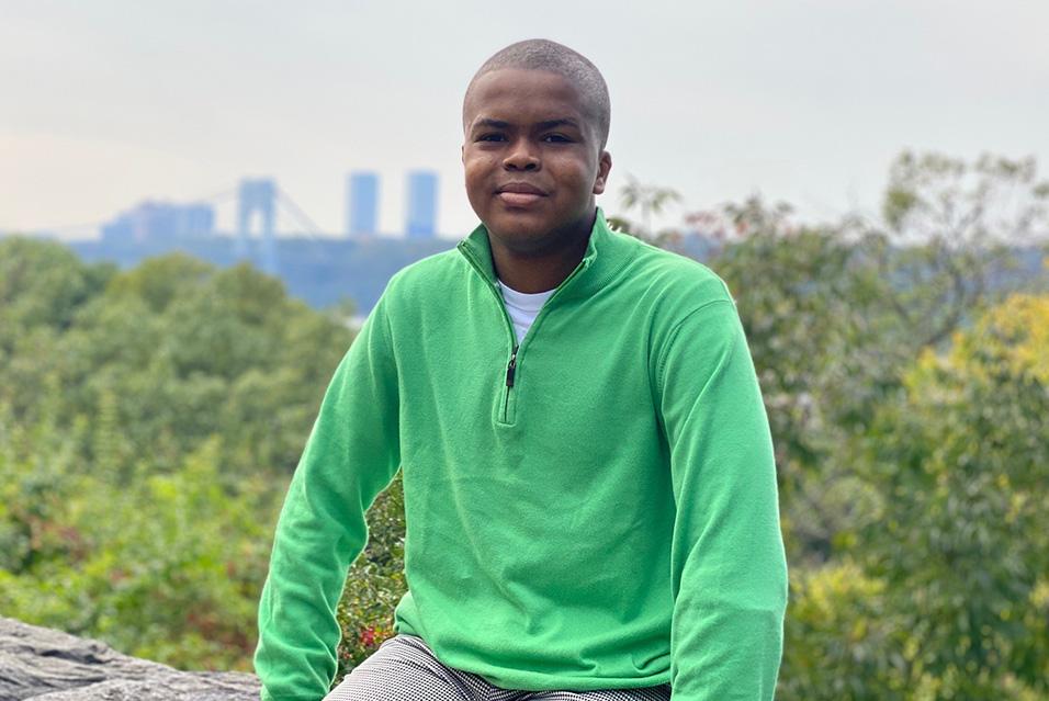 Mo Campbell (a young Black man) sits outdoors in a scenic location, smiling at the camera. 