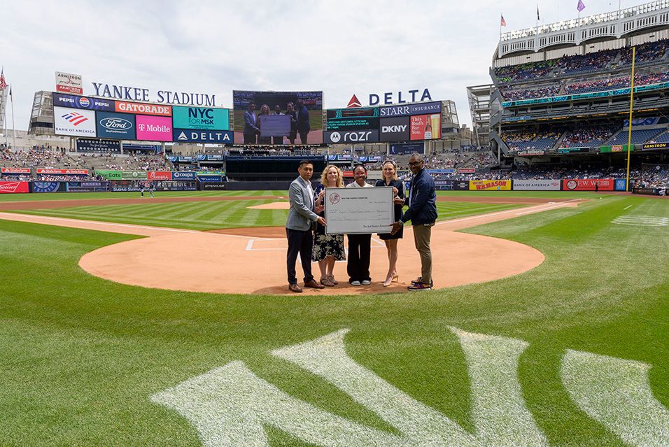 A group of people stand at home plate in Yankee Stadium, holding a large check and smiling. 